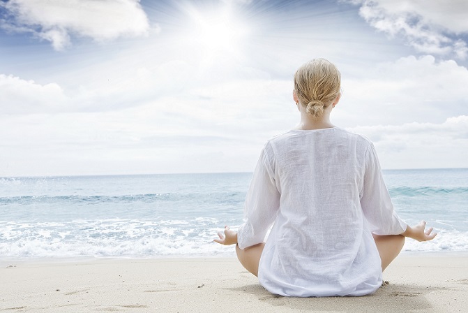 Image of the back of a lovely blond woman meditating at the beach with the sparkling ocean.